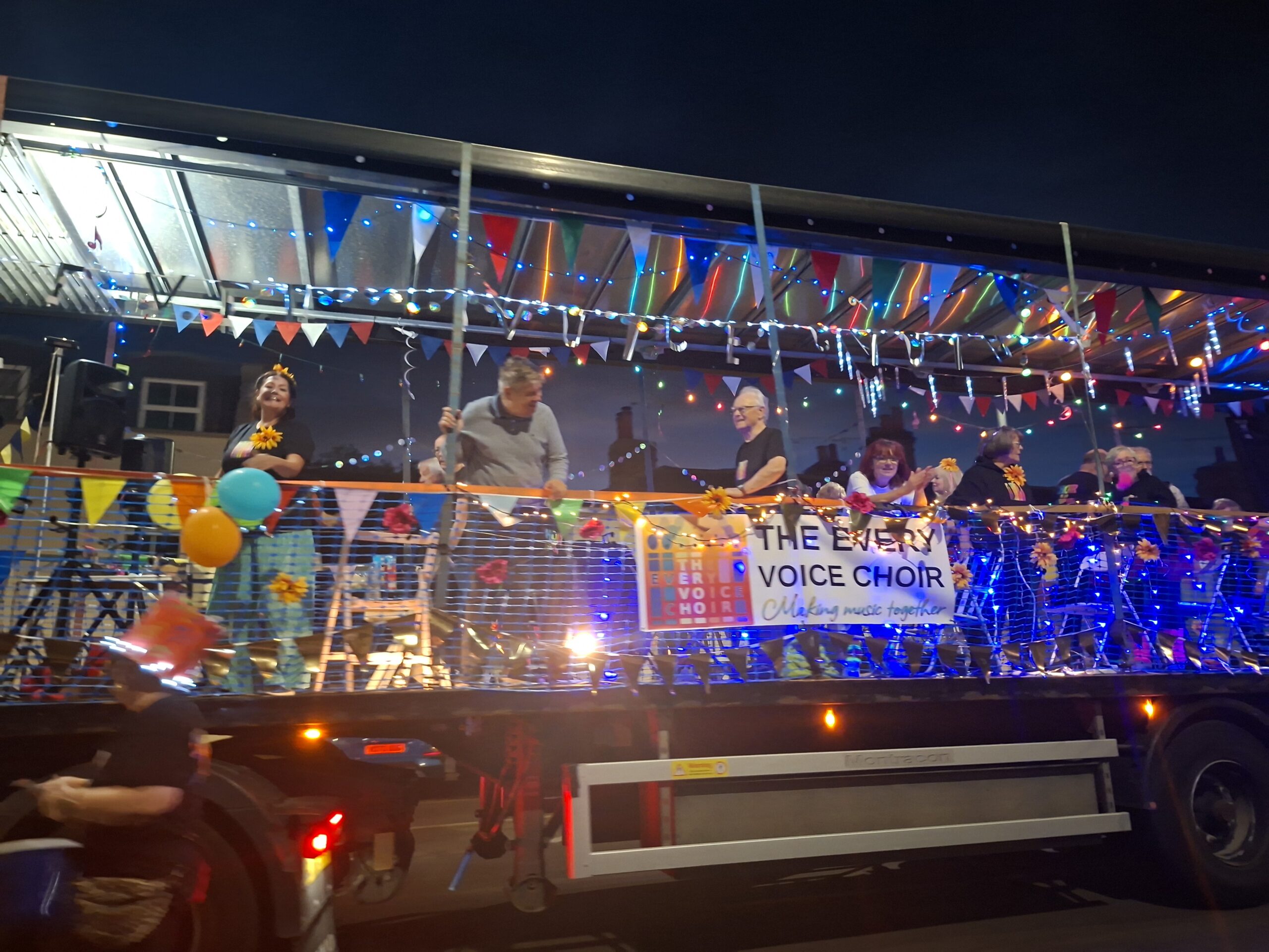 The Every Voice Choir taking part on a colourful illuminated carnival float